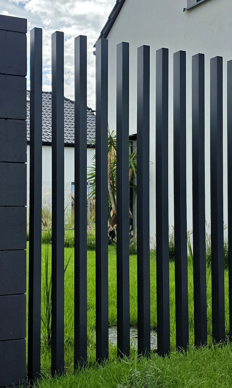 Nowoczesne ogrodzenie frontowe z pionowych profili i grafitowych bloczków